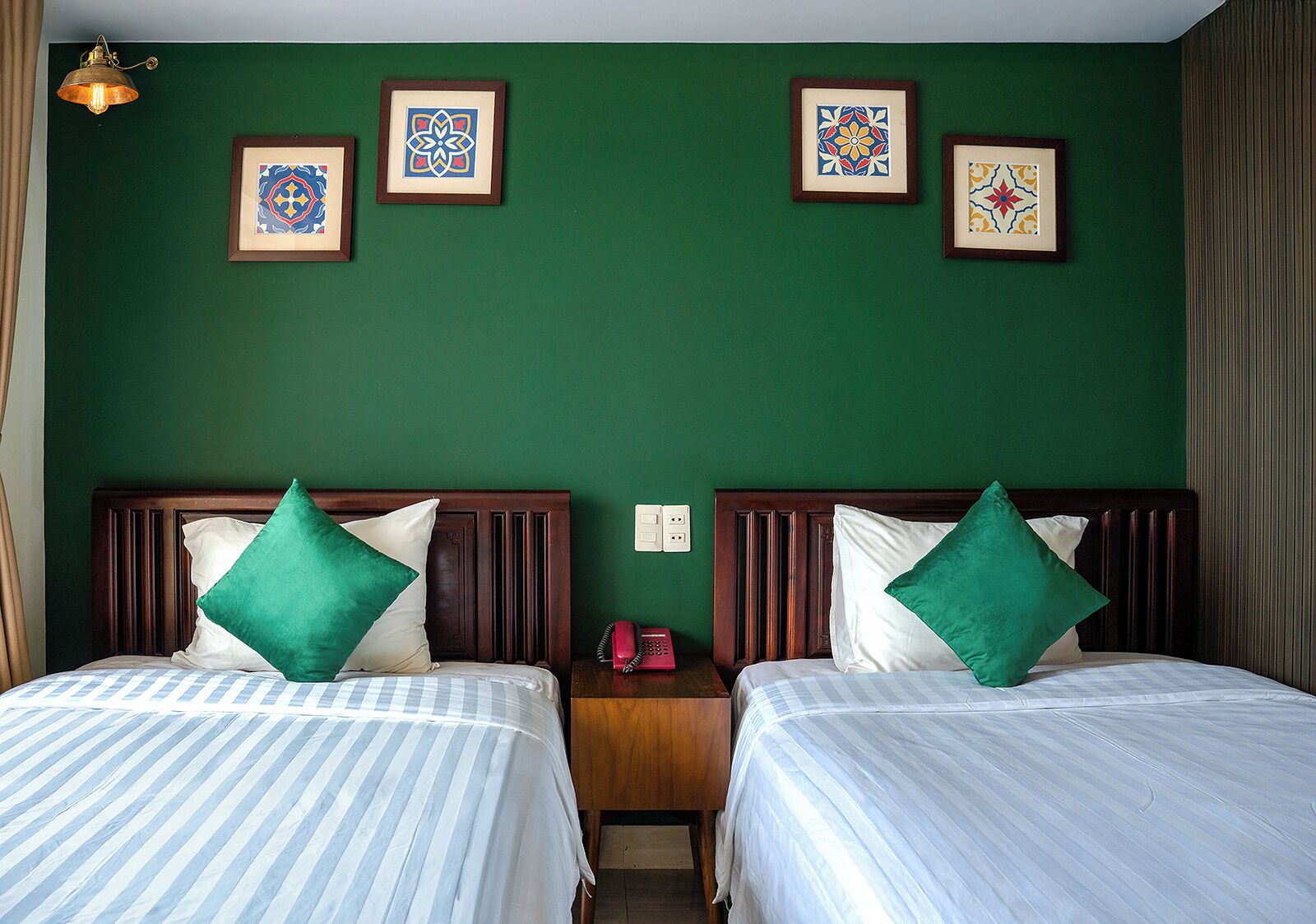 Een hotelkamer met twee bedden, groene wanden en kunstwerken in lijsten.