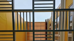Ein gelbes Gebäude mit vergittertem Fenster, einer kleinen Leuchte und einer Treppe.