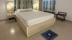 A bedroom with a bed, nightstands, an air conditioning unit, curtains, a wall-mounted light, and a small wooden chair.
