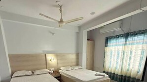 A hotel room with two beds, a ceiling fan, an air conditioning unit, and a window with curtains.