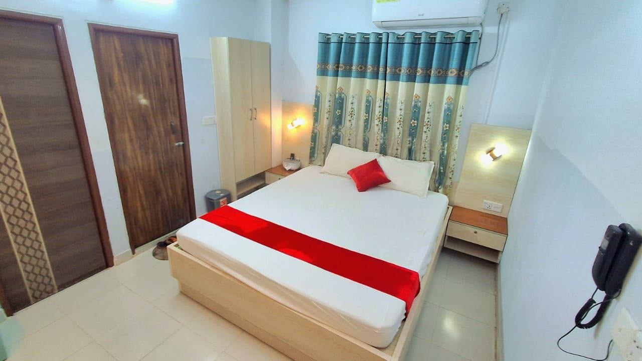 Une chambre d’hôtel comprenant un lit, une armoire, une table de chevet, un téléphone et un rideau.