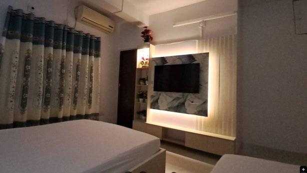 A hotel room with a bed, a TV mounted on the wall, and a shelf with decorative items.