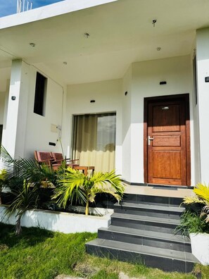 A modern building with a wooden door, a small porch with steps, and potted plants.