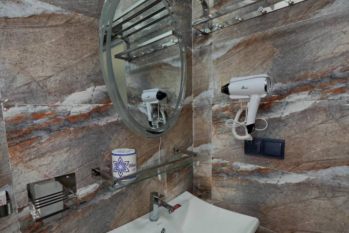 A bathroom with a marble wall, a sink, a mirror, and two hair dryers mounted on the wall.