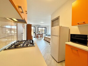 A modern kitchen with a gas stove, a refrigerator, and a microwave. There is a dining area with a table and chairs in the background. - " Comfort Apartments " (Bari Sardo)