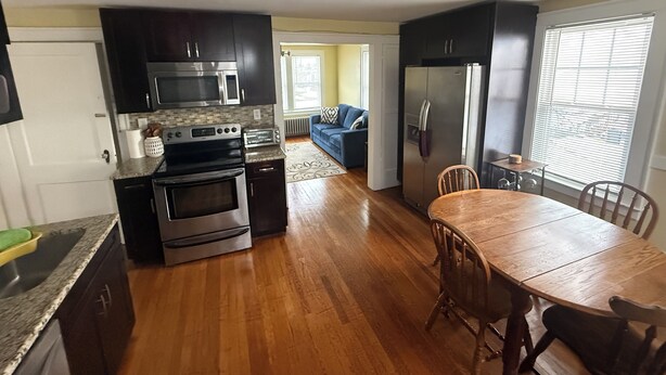 Una cocina compacta con armarios oscuros, electrodomésticos de acero inoxidable y una mesa de comedor de madera.