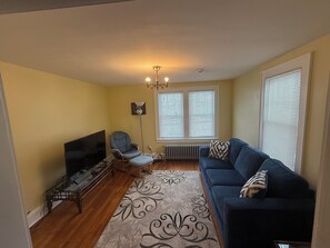 A living room with a TV, a blue sofa, a chair, and a patterned rug.