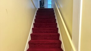 Una escalera con peldaños alfombrados de rojo que conduce a una puerta.