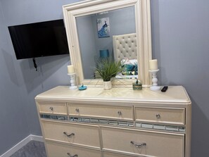 A beige vanity with a mirror, two candles, a remote control, and decorative items. - Cozy 1-bedroom house in beautiful North Palmetto Point with AC. (North Palmetto Point)
