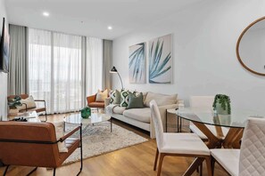 Een moderne woonkamer met een bank, stoelen, een glazen salontafel en kunst aan de muur.