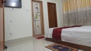 Un dormitorio con cama, televisor, puerta con panel decorativo, unidad de aire acondicionado y ventana con cortinas.