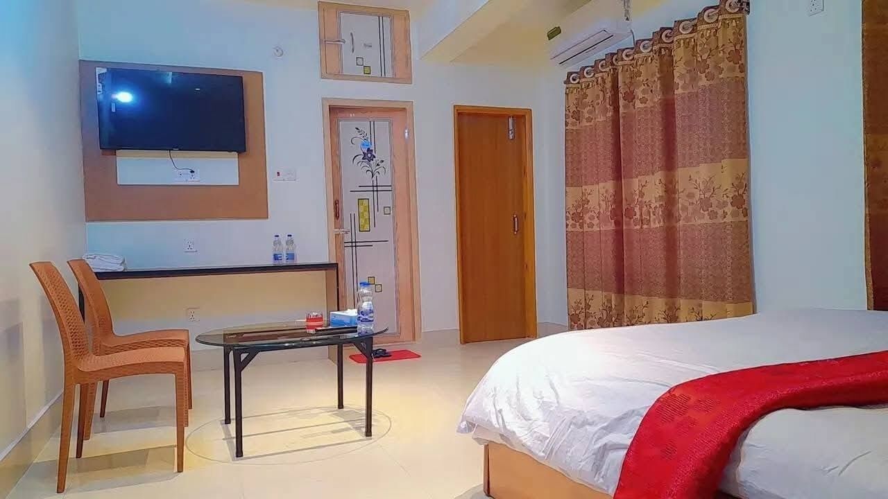 Habitación de hotel con cama, televisor montado en la pared, una mesita con una silla y una puerta con diseño decorativo.