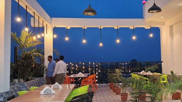 Un espacio al aire libre para comer con mesas y sillas, plantas en macetas e iluminación colgante.
