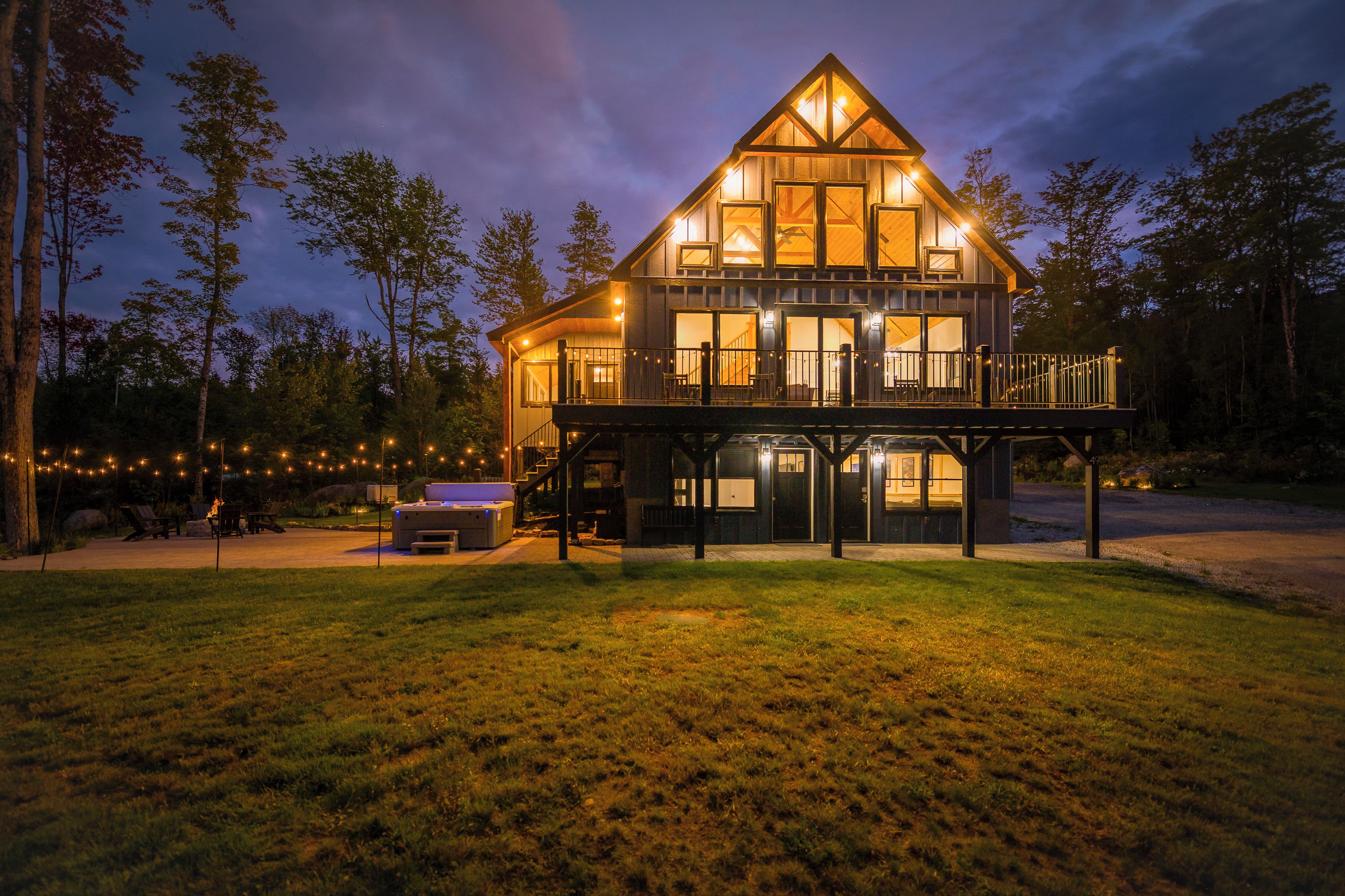 A two-story wooden house with a balcony, surrounded by trees and a grassy yard.