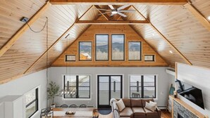 Un habitación estilo loft con techo inclinado, ventanas amplias, chimenea y zona de comedor.