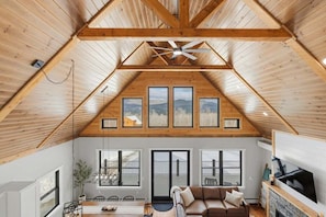 A loft-style room with a sloped ceiling, large windows, a fireplace, and a dining area. - Mt Chalet- Views, Hot Tub, Fireplace, Golden Tee (Bethel)