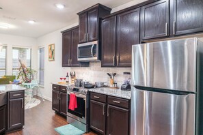 Una cocina moderna con armarios de madera oscura, electrodomésticos de acero inoxidable y un tapete azul verdoso.