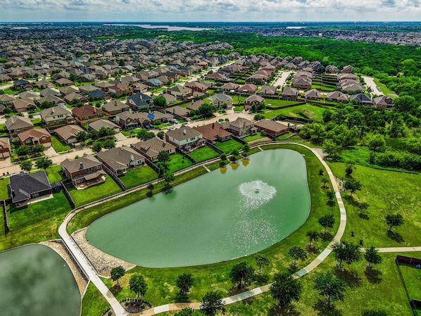 Vista aérea de una zona residencial con casas, un estanque central y un parque circundante.