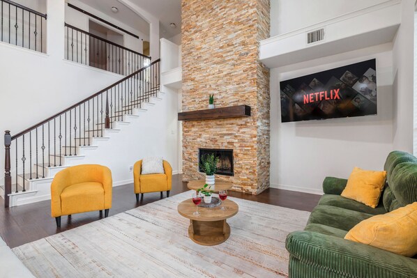 Un amplio salón con chimenea, una escalera, un sofá verde y un televisor de pantalla plana.