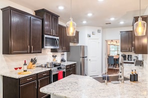 A kitchen with dark wood cabinets, a stainless steel refrigerator, a microwave, and a granite countertop. - Spacious 6-bedroom house in charming Little Elm with King beds (Little Elm)