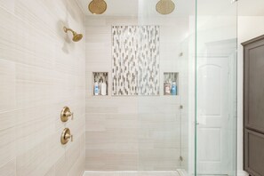Un baño moderno con azulejos blancos, una cabina de ducha de vidrio y un armario de madera.