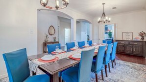 Une salle à manger avec une longue table dressée pour six personnes, des chaises bleues et deux lustres.