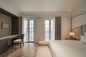 A hotel room with a bed, a desk, a chair, a nightstand with a lamp, and large windows with a view of the city. - Thai Hoang Residence - 15 Thai Phien (Hanoi)