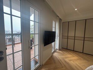 A spacious room with a large sliding glass door leading to an outdoor area, a flat-screen TV mounted on the wall, and a herringbone-patterned wooden floor. - Thai Hoang Residence - 15 Thai Phien (Hanoi)