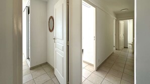 Ein Flur mit weißen Wänden und Fliesenboden, der zu einem Raum mit einer weißen Tür und einem Spiegel an der Wand führt.