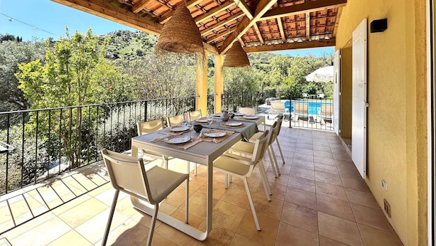 Ein Außenbereich mit Essplatz, einem Pergola-Dach, einem Pool im Hintergrund und Blick auf die umliegende Landschaft.