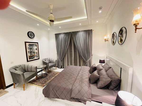 Ein modernes Schlafzimmer mit Bett, Sessel, kleinem Tisch und Deckenventilator.