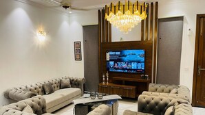 A modern living room with a large flat-screen TV, tufted sofas, a coffee table, and a chandelier.