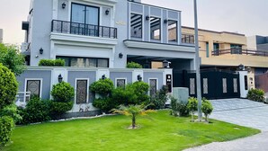 A modern two-story building with a balcony, a well-maintained lawn, and a gated entrance.