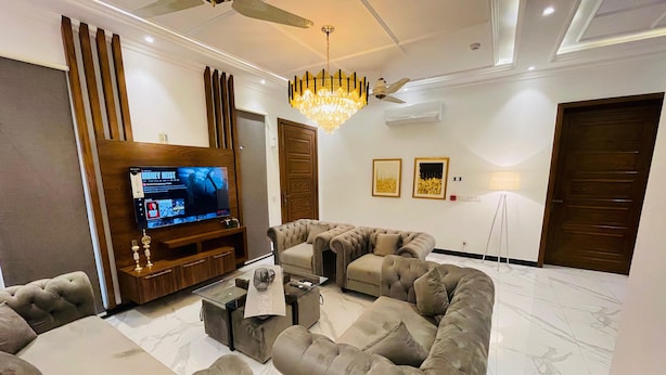A modern living room with a sectional sofa, a flat-screen TV, a chandelier, and a ceiling fan.