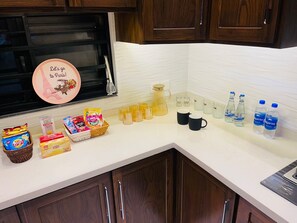 A kitchen counter with various food items, a coffee maker, and water bottles. - Luxurious House 2 BHK Phase 5 DHA Near Raya & Airport (Lahore)