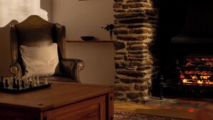 Une pièce chaleureuse avec une cheminée en pierre, un fauteuil en cuir et un jeu d’échecs posé sur une table en bois.