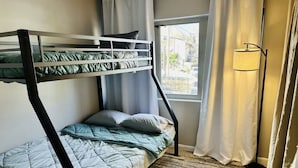 A bunk bed with a green and white quilt, a window with curtains, and a floor lamp.