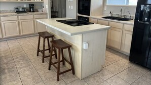 A modern kitchen with a central island, bar stools, a black refrigerator, and a window providing natural light.