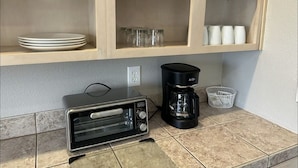 A kitchen with a toaster, coffee maker, and shelves with glassware and plates.