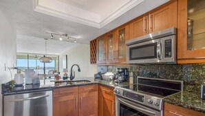A modern kitchen with stainless steel appliances, wooden cabinets, and a granite countertop. - Unforgettable Water Views! On the Sand at Island's End! Heated Pool, Free Parking & Beach Gear! (Fort Myers Beach)