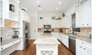 A modern kitchen with white cabinetry, granite countertops, stainless steel appliances, and a central island.