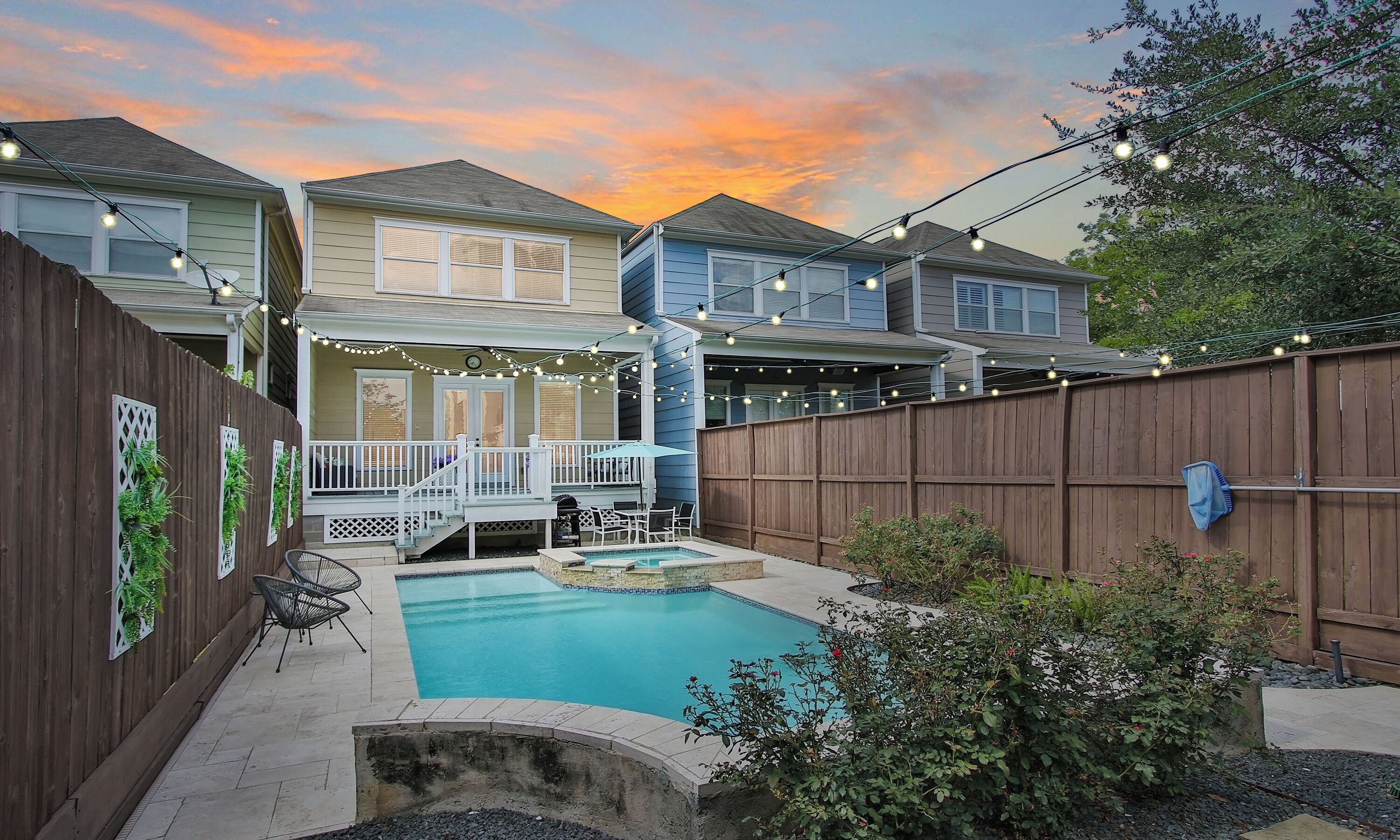 A residential backyard with a swimming pool, a wooden deck, and string lights.
