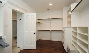 A walk-in closet with white shelving, a door, and a wooden floor.