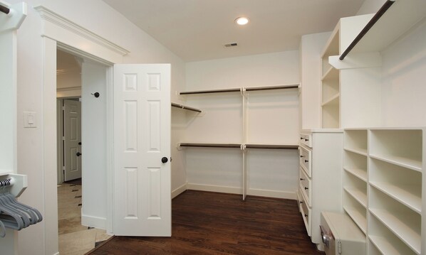 A walk-in closet with white shelving, a door, and a wooden floor.