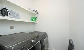 A laundry room with an LG inverter direct drive washer and dryer, a green water heater, and a white shelf with a hairdryer and a green box.