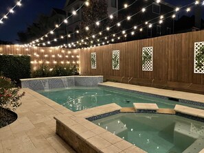 A swimming pool with a tiled edge, surrounded by a wooden fence with lattice panels, and string lights overhead. - Downtown Houston-Private Pool, Hot Tub & Game Room (Houston)
