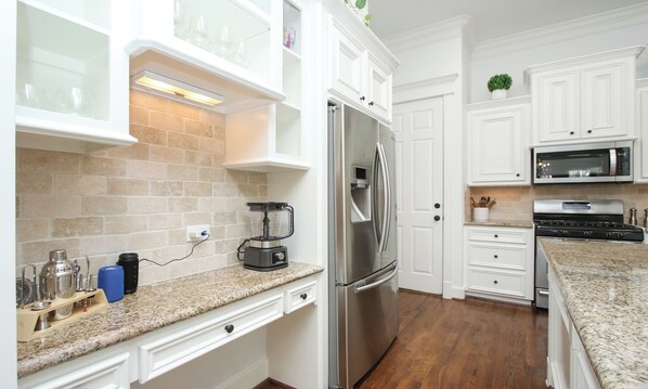 Una cocina moderna con armarios blancos, encimeras de granito, un refrigerador de acero inoxidable, horno empotrado y microondas.