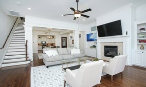 A spacious living room with a staircase, a fireplace, and a kitchen in the background. - Downtown Houston-Private Pool, Hot Tub & Game Room (Houston)