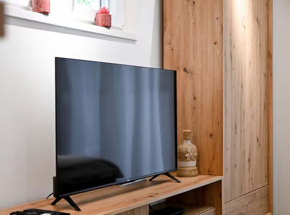 Ein Flachbildfernseher auf einem Holzständer in einem Raum mit einer Holzwand und einem Regal darüber.