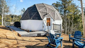 Une structure en forme de dôme géodésique, dotée d’une terrasse en bois et de chaises Adirondack bleues.